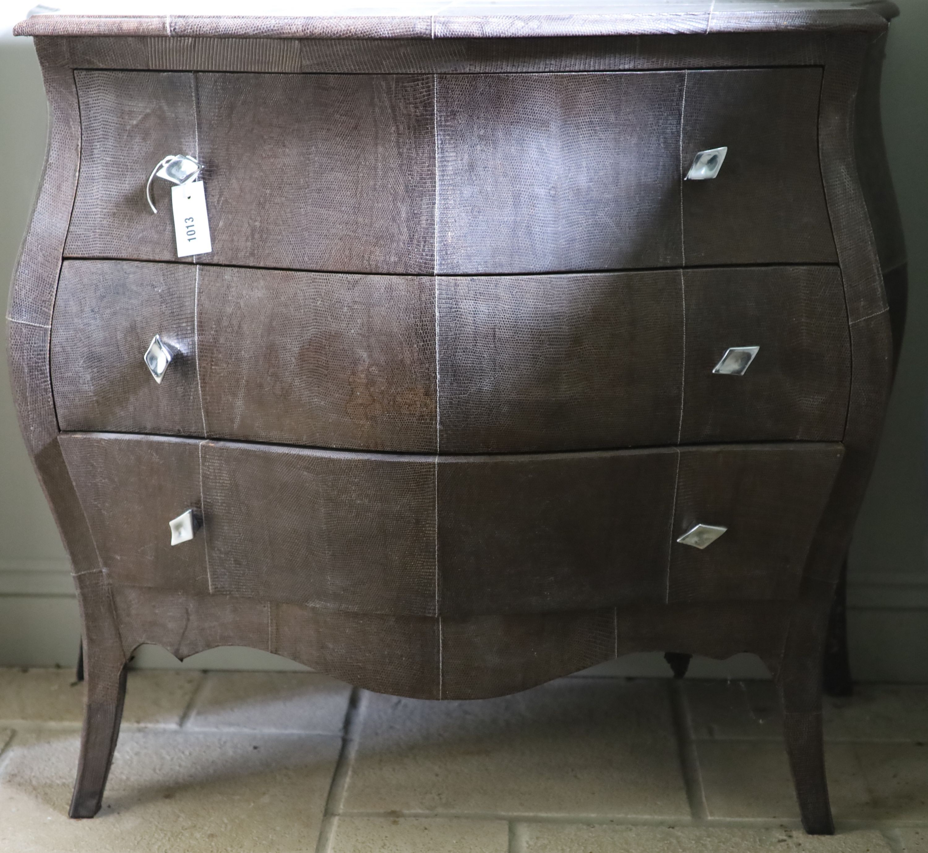 A three drawer bombe commode, upholstered in simulated snake skin, width 102cm depth 51cm height 88cm